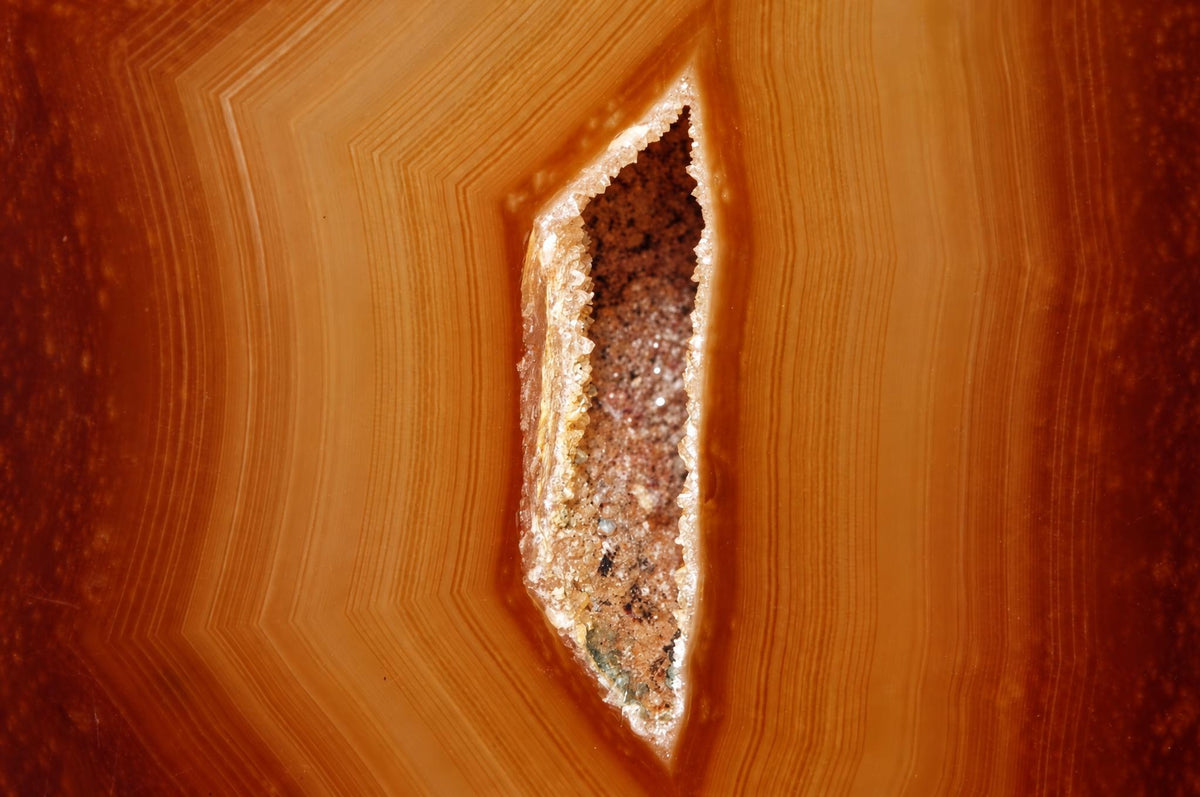A polished agate slice with concentric bands of orange and brown, featuring a central cavity lined with crystals.