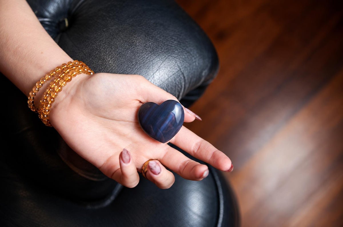 A hand holds a polished, dark blue heart-shaped stone on a black leather surface.