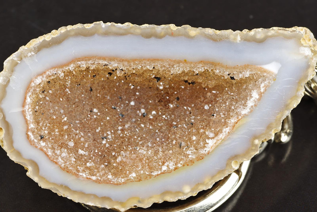 A sliced agate geode with a white outer band and a brown, crystalline inner cavity sits on a dark surface.