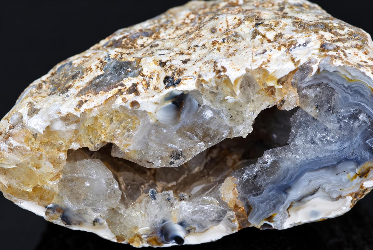 A cut agate nodule shows grey bands and rough crystal cavities within a pale brown outer crust.