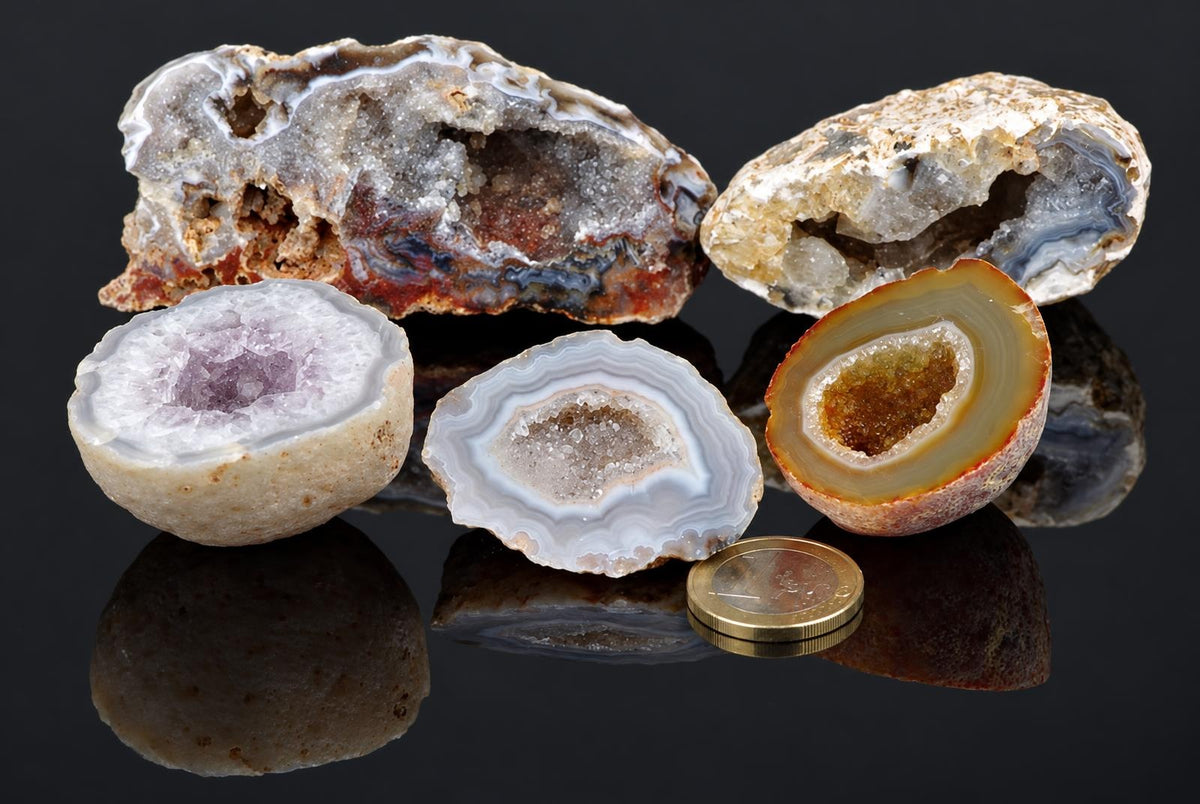 Open agate nodules with banded edges and crystal-filled centres are arranged beside a coin on a dark reflective surface.