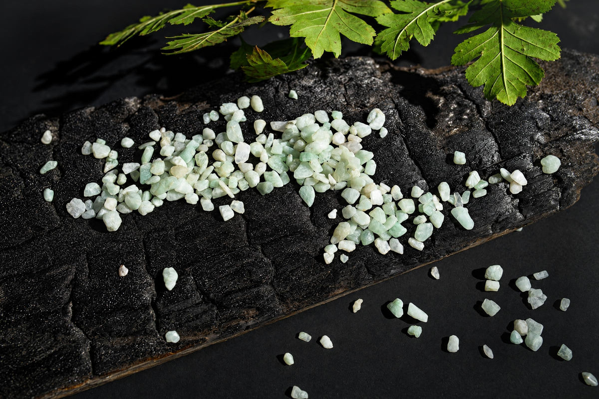 Pale mint-green stone chips are scattered over a dark textured surface beneath green leaves.