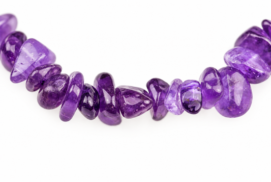 A strand of polished, irregularly shaped purple amethyst chips arranged in a loose curve on a white surface.
