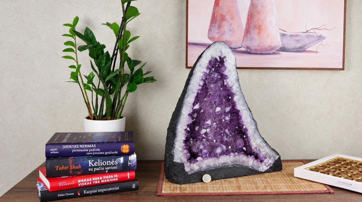 A large amethyst geode with purple crystals inside, resting on a dark base and placed on a wooden surface.