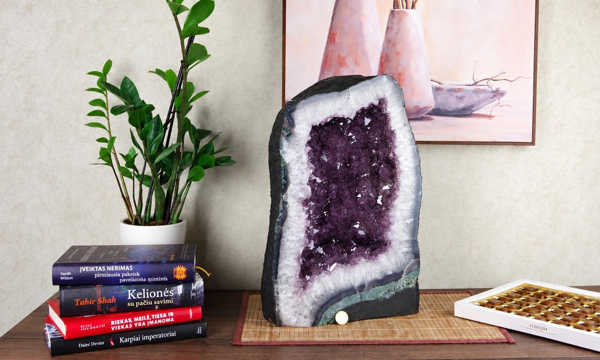 A large amethyst geode with purple crystals inside a white and dark outer shell stands on a wooden surface.