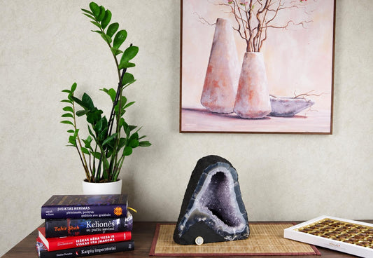A large, dark geode with a purple crystal interior sits on a bamboo mat next to books and a plant.
