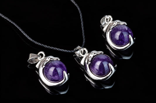 Three silver-toned pendants with round purple stones on a dark surface.