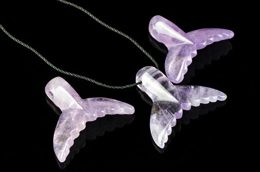 Three translucent purple dolphin-tail pendants on a dark surface, each with scalloped edges and a green cord.