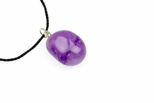 A polished purple amethyst pebble pendant on a black cord with a silver-toned bail, set against a white background.