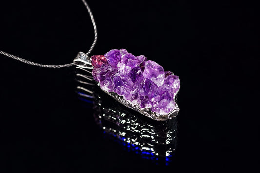 A silver-toned pendant with a cluster of purple amethyst crystals on a dark reflective surface.