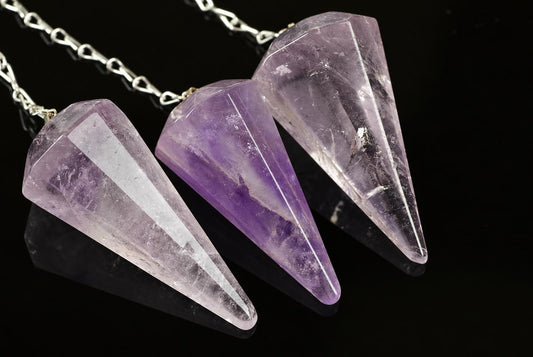 Three silver-toned chains hold faceted amethyst pendulums in pale and deep purple hues on a dark reflective surface.