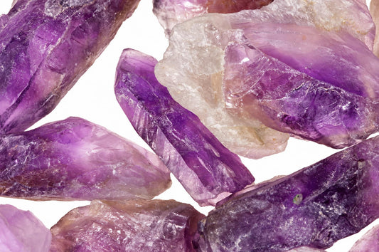 Several raw amethyst crystals with purple and clear facets arranged on a white surface.