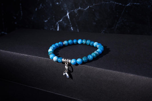 A bracelet with round blue beads and a silver heart charm rests on a dark surface.