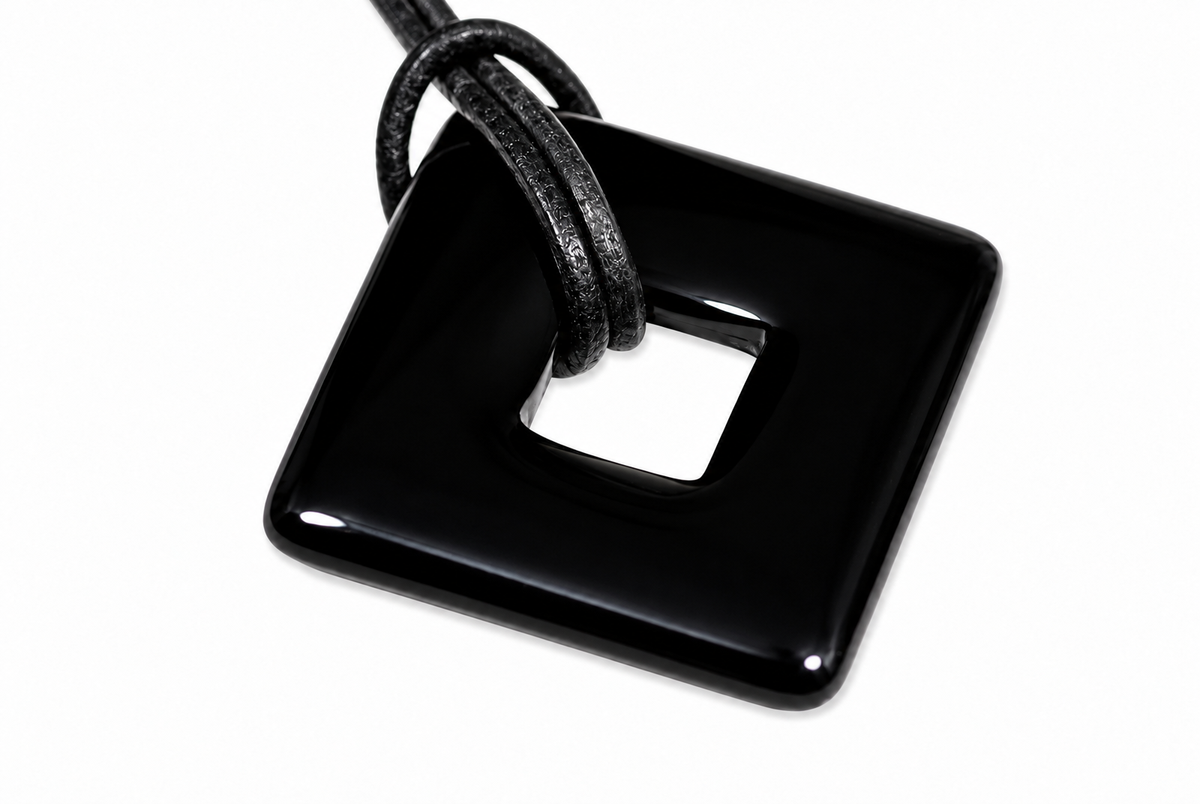 A glossy black square pendant with a central hole, threaded by a textured black cord against a white background.