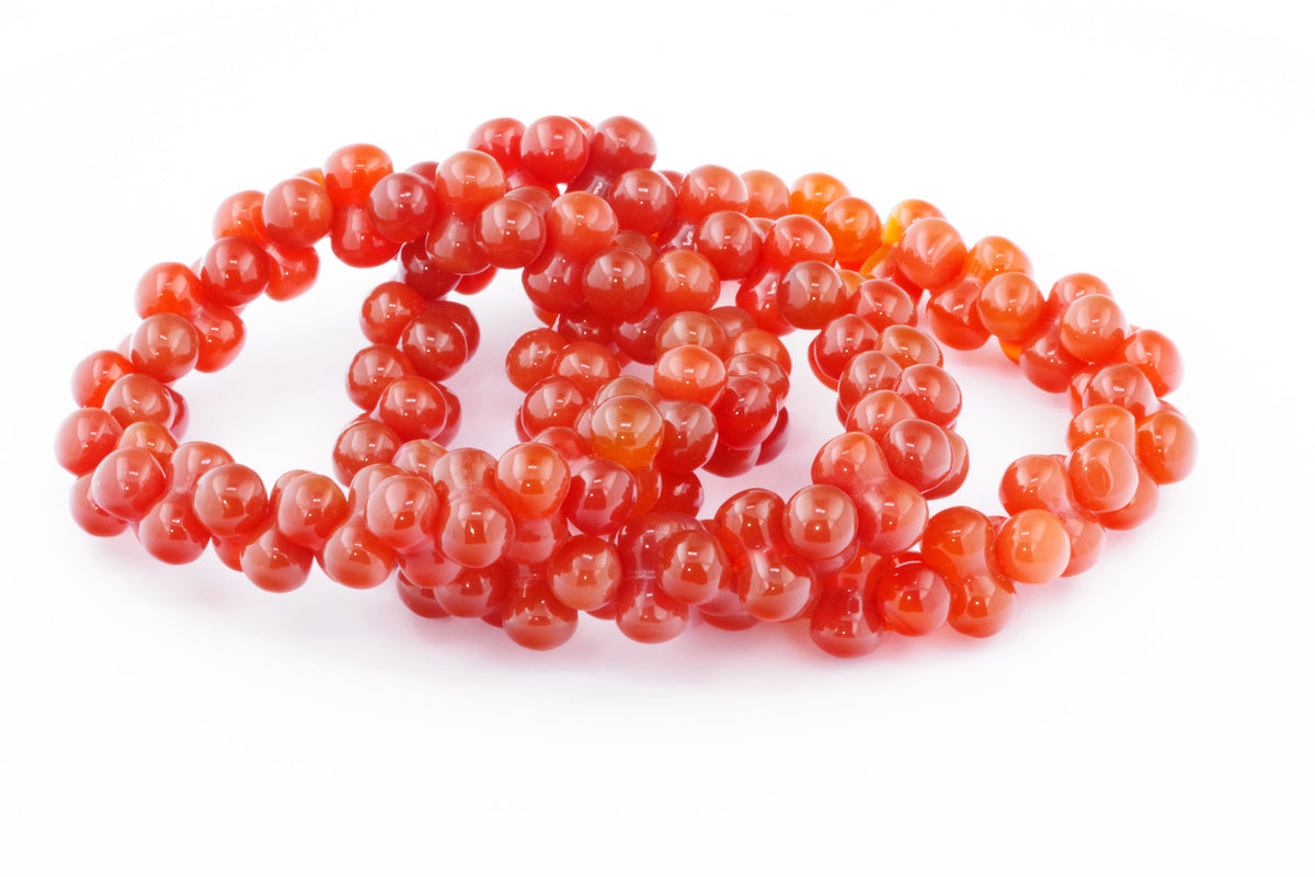 Carnelian bracelet – DNA made of polished natural carnelian crystal beads in a vibrant orange-red hue, laid on a white background.