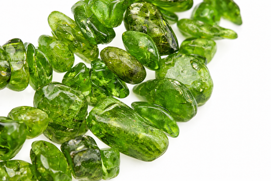 A pile of polished, translucent green diopside chips on a white surface.