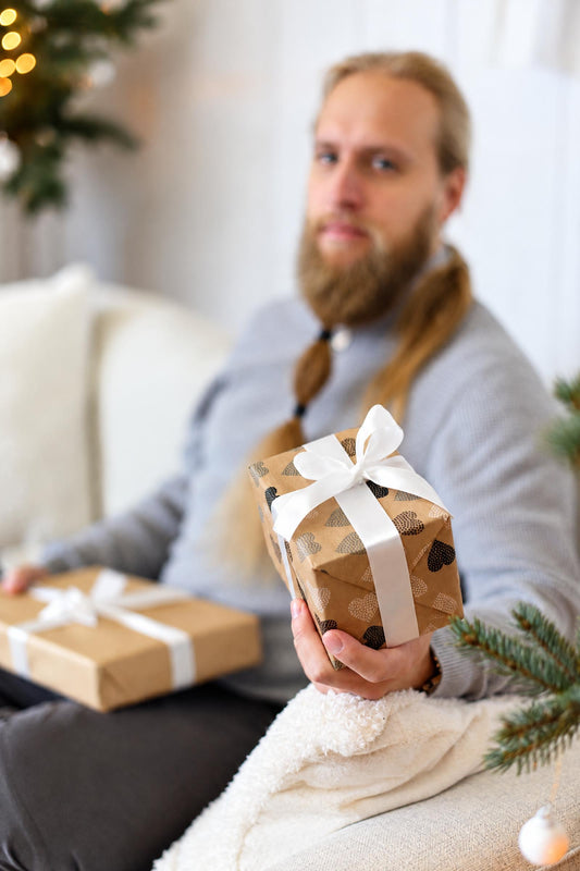A man holds a small gift wrapped in brown paper with black hearts and a white ribbon.
