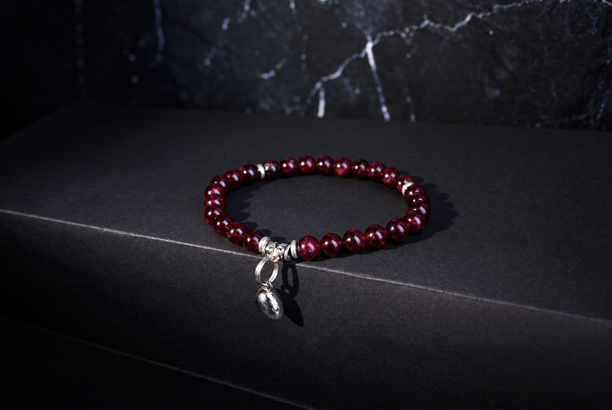 A bracelet with round red beads and a silver heart charm rests on a dark surface.