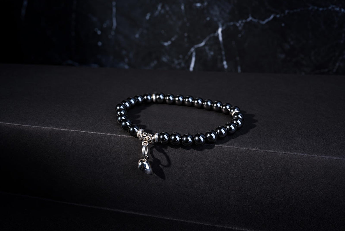 A black beaded bracelet with silver accents and a small heart-shaped charm rests on a dark surface.