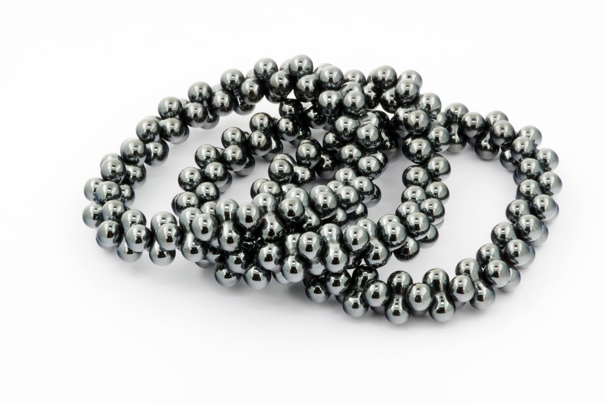 Close-up of polished dark metallic beads forming a looped Hematite bracelet – DNA, showcasing smooth natural crystals with a reflective surface for healing and grounding purposes.