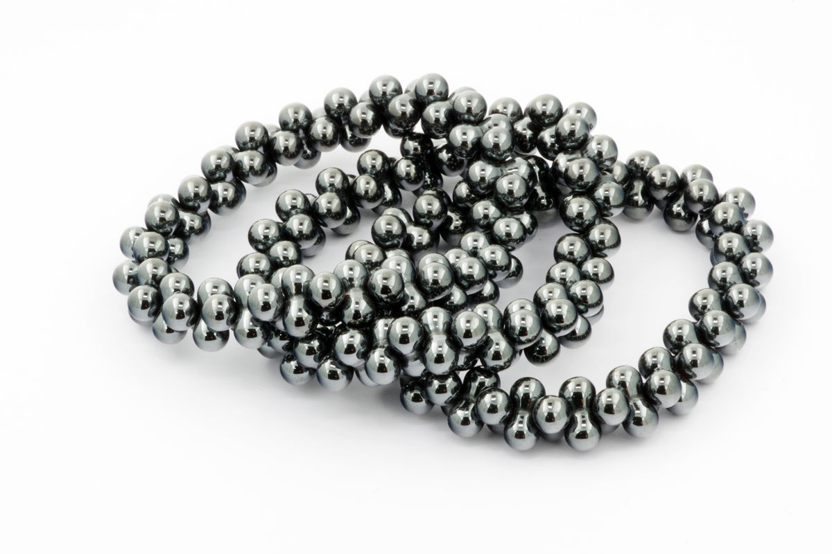Close-up of polished hematite beads arranged in overlapping strands, showcasing the smooth, reflective surface and metallic grey color of the Hematite bracelet – DNA.