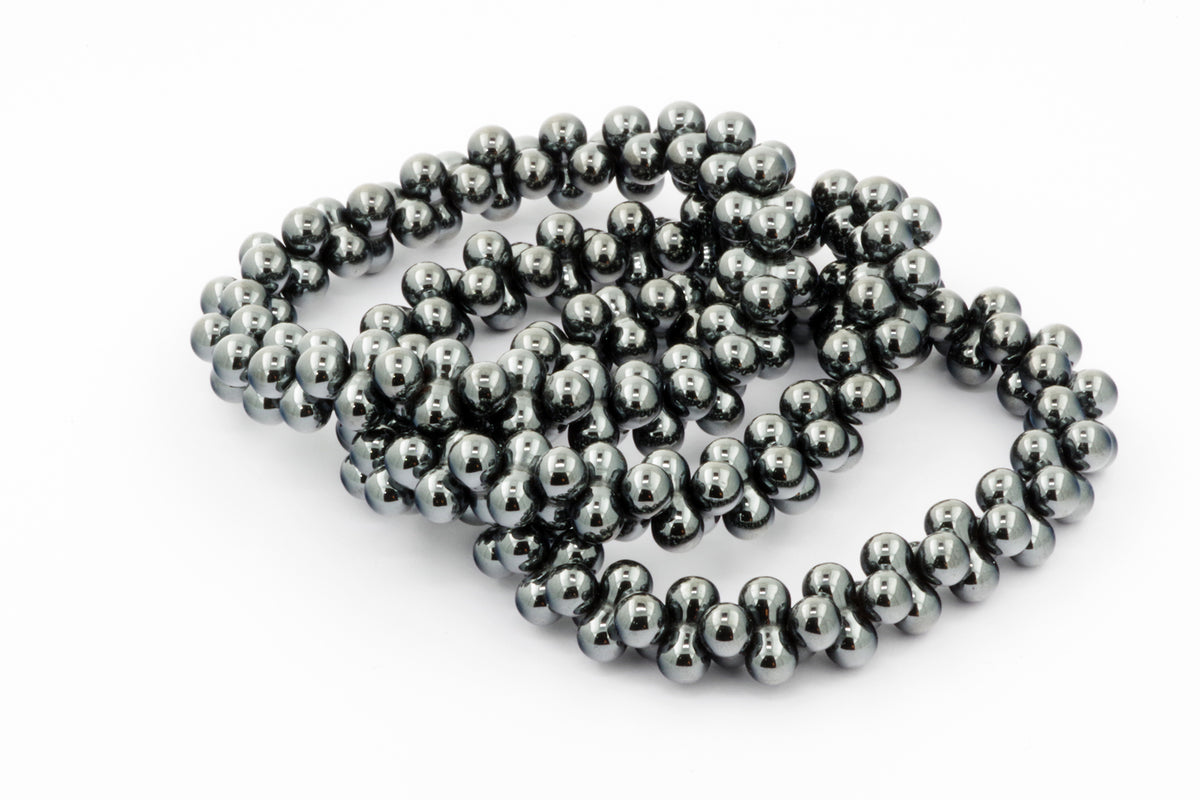 Close-up of polished dark metallic hematite beads arranged in a continuous loop, showcasing the smooth, reflective surface of the Hematite bracelet – DNA against a white background.