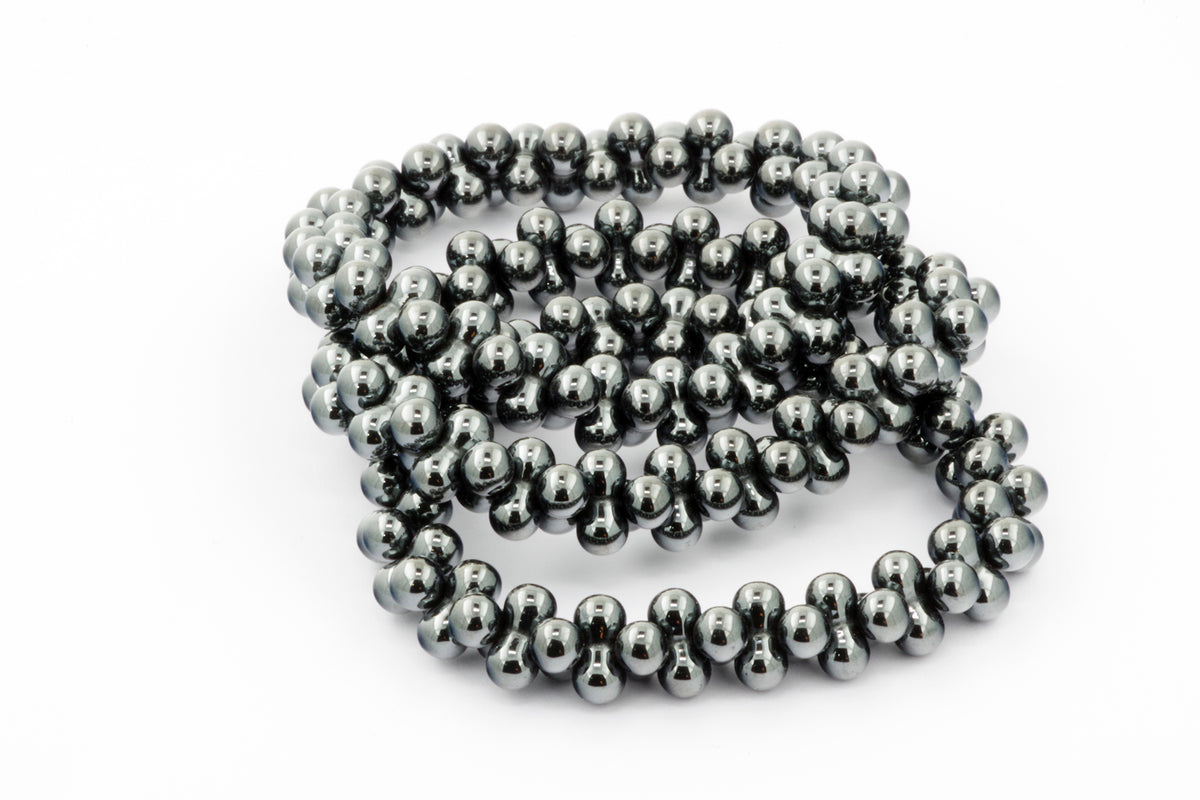 Close-up of a polished dark metallic bead necklace arranged in a loose coil, showcasing the reflective hematite beads of the Hematite bracelet – DNA.