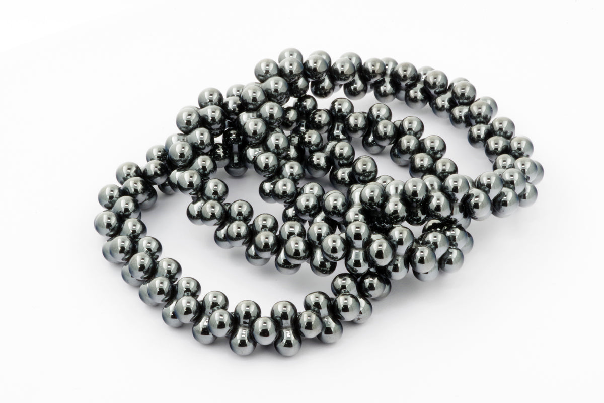 Close-up of polished dark gray hematite beads arranged loosely to form Hematite bracelet – DNA, showcasing natural crystal luster and smooth surface texture.
