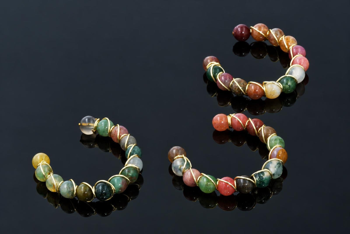 Open circular rings of colourful polished beads wrapped in gold-coloured wire rest on a dark reflective surface.