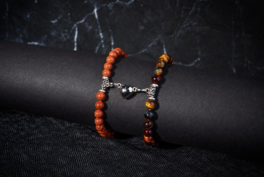 Orange and striped brown-and-gold beaded bracelets joined by a silver-tone heart charm on a black display.