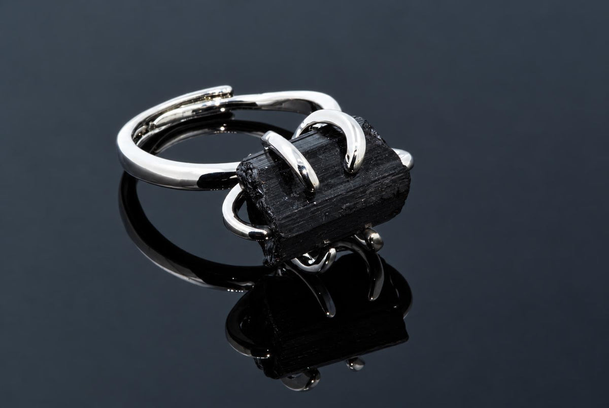 A silver-tone ring holds a rough black crystal with lengthwise ridges on a dark reflective surface.