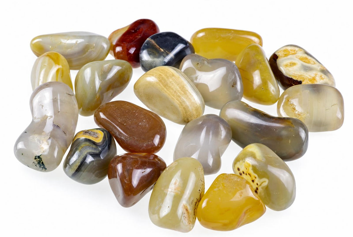 A collection of polished agate stones in various shapes and colours including yellow, brown, grey, black and white on a pale surface.