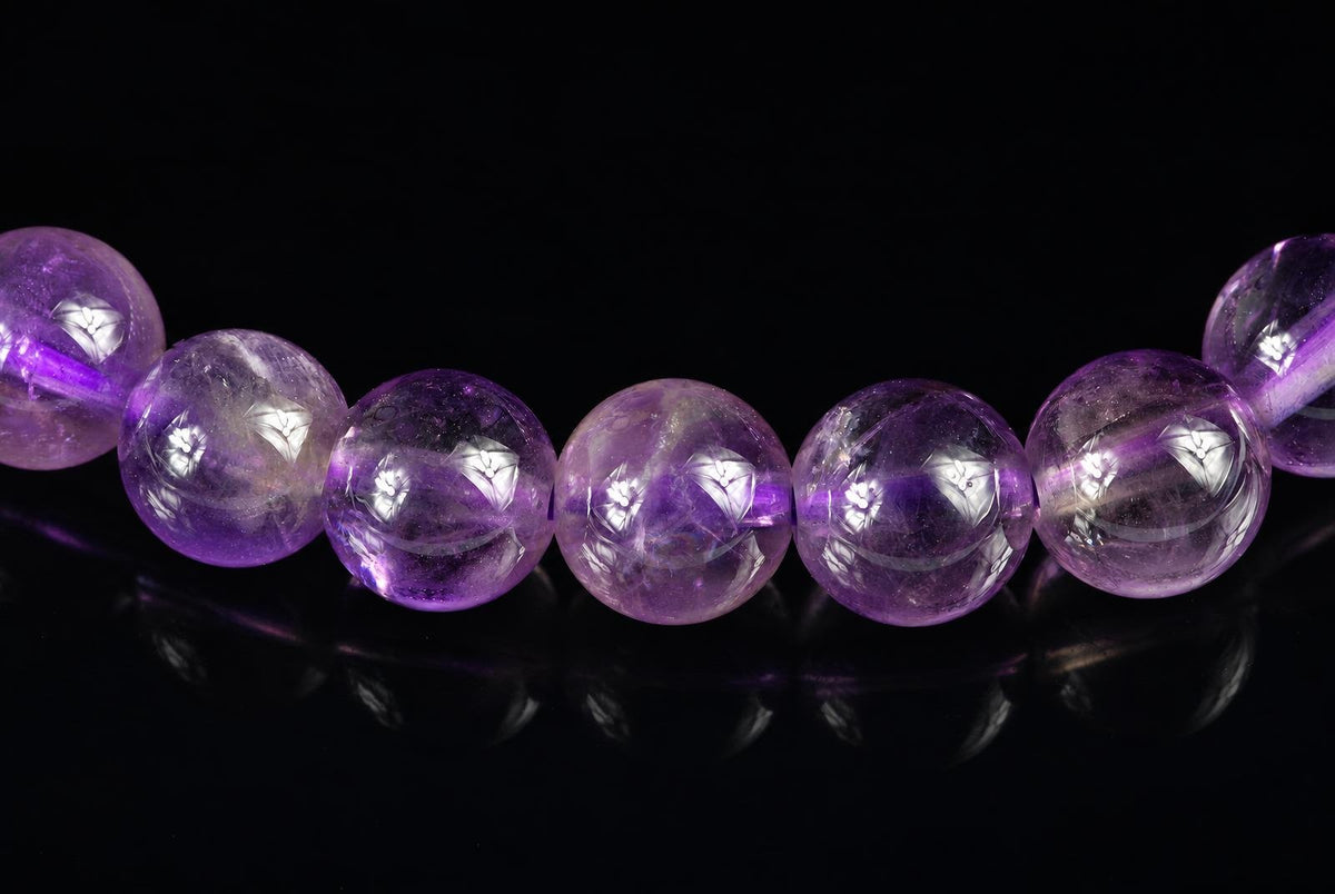 A row of round, purple amethyst beads with white floral inlays on a dark reflective surface.