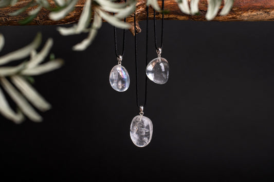 Three clear, smooth quartz pendants hang from black cords against a dark background with pale foliage.