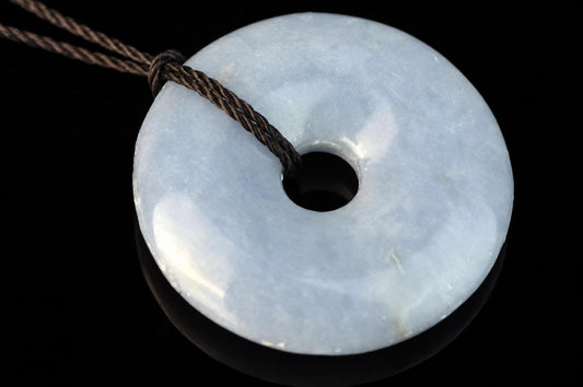 A light blue, polished donut-shaped pendant with a central hole, threaded on a dark brown cord against a black background.