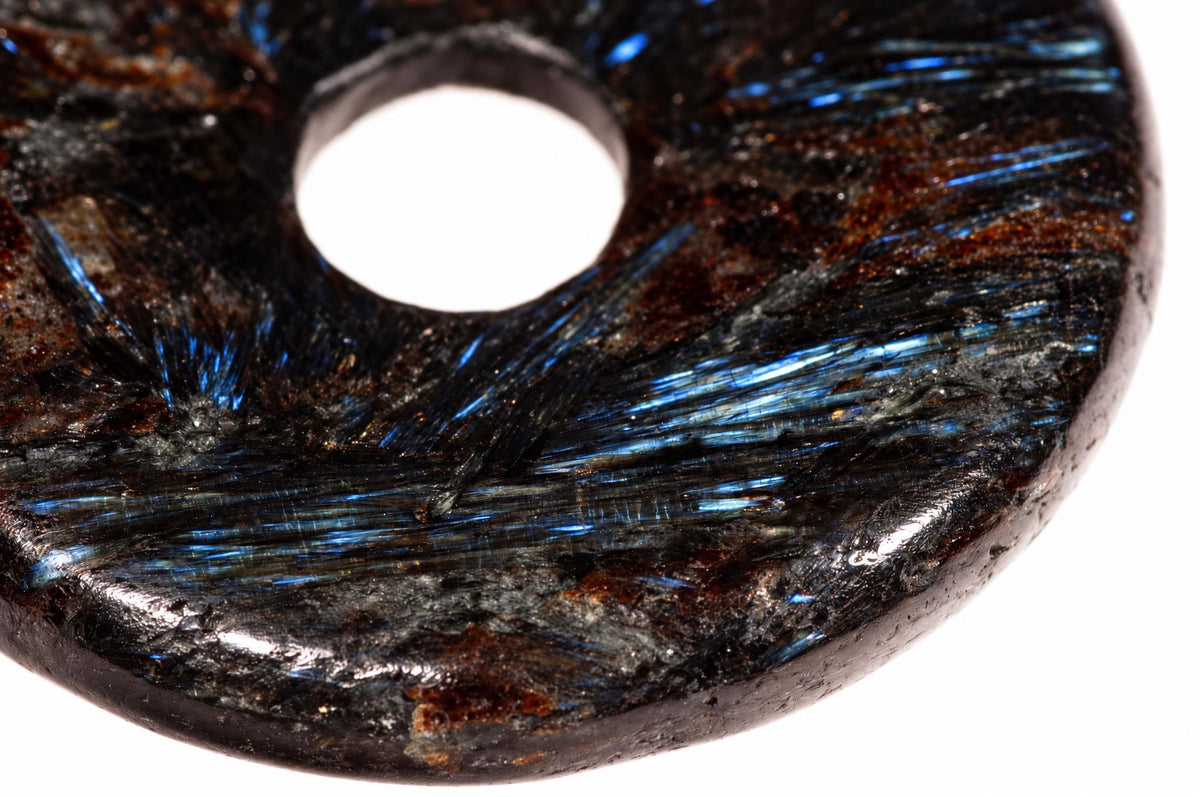 A polished, dark brown donut-shaped pendant with a central hole and visible blue metallic inclusions on a white surface.