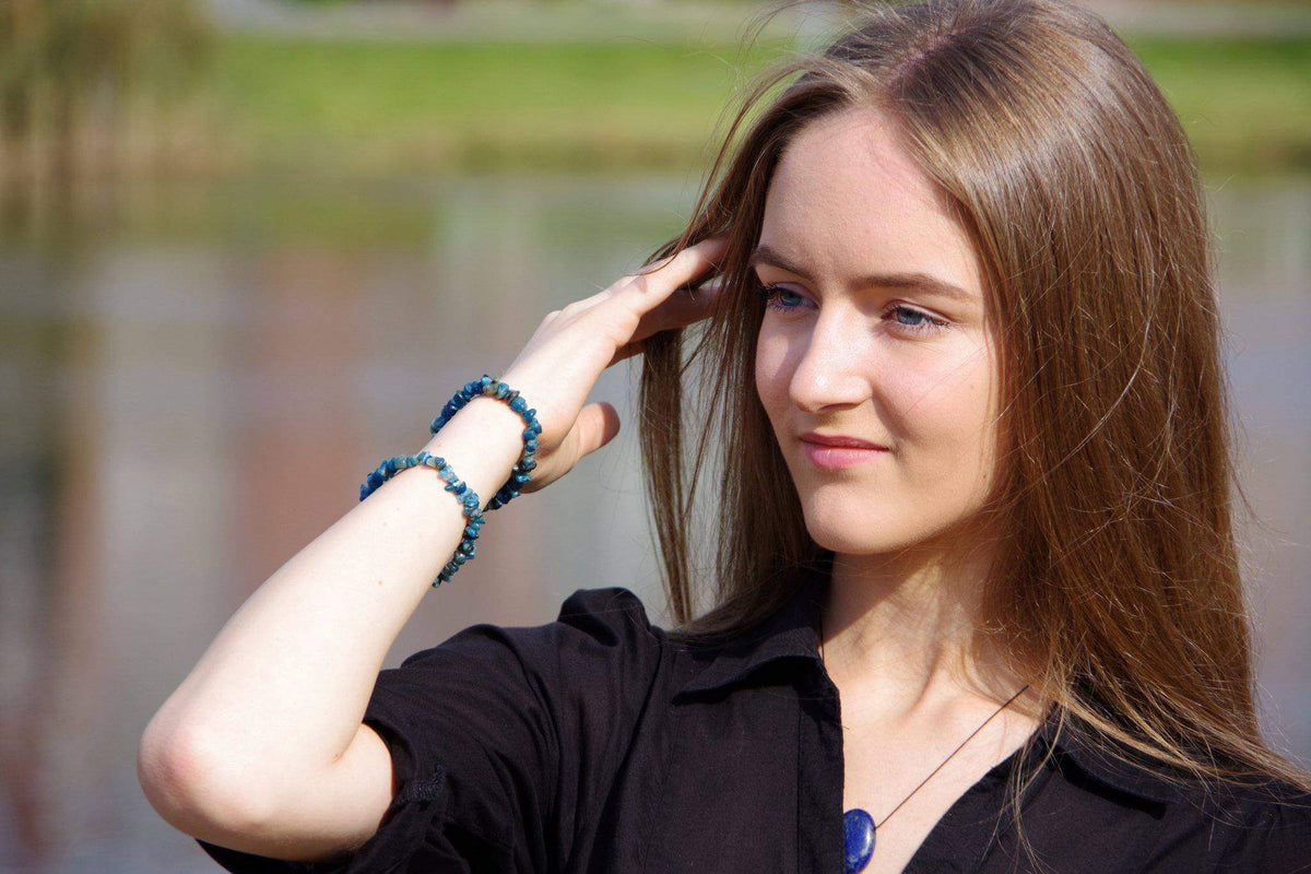 Young woman outdoors wearing a blue stone necklace and two matching Apatite bracelet – Chips on her wrist, showcasing crystal jewellery in natural sunlight.