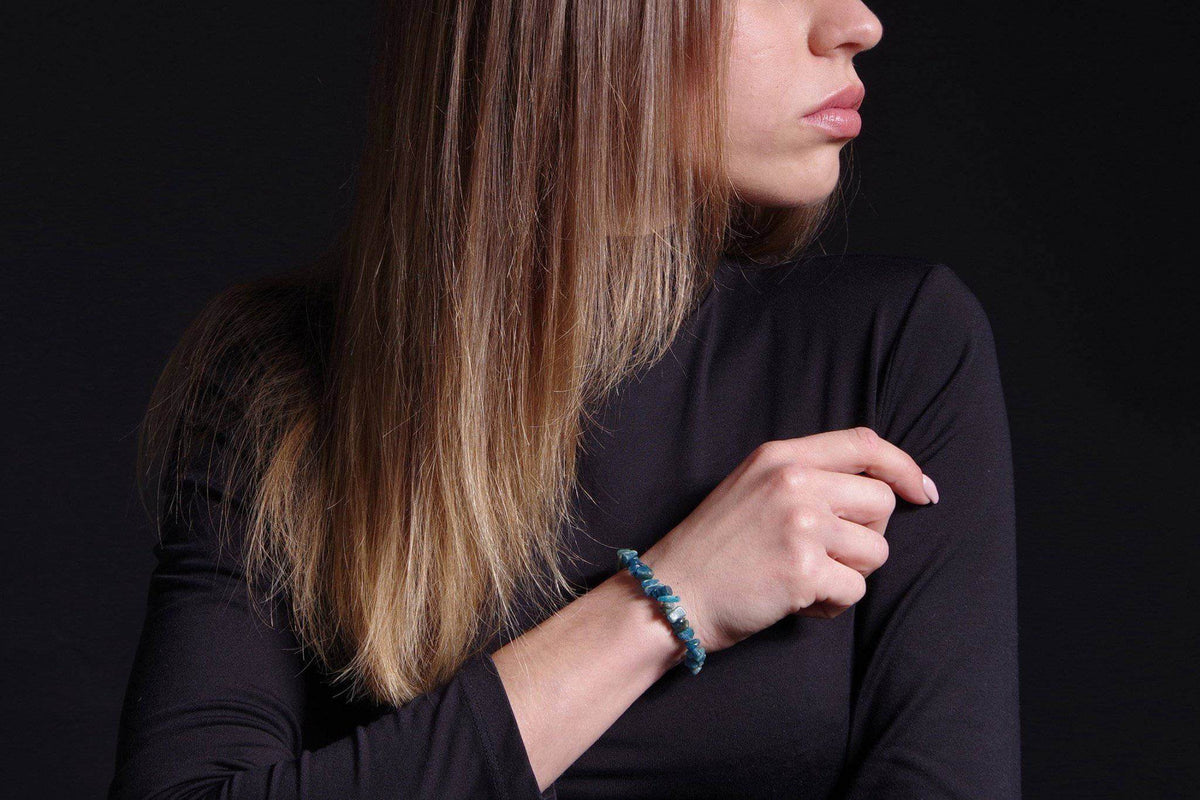 A woman wearing an Apatite bracelet – Chips on her wrist, showcasing blue-green irregular chip-shaped crystals against a black long-sleeve top.