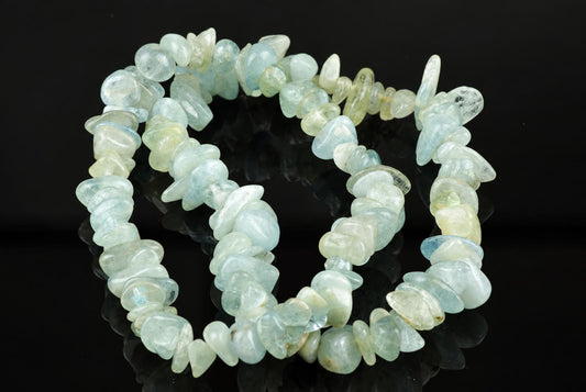 A bracelet made of irregular chips in pale blue, green and white tones on a dark reflective surface.