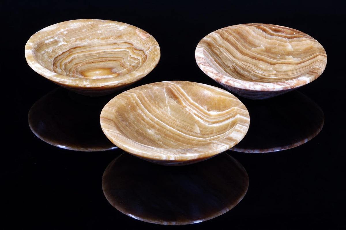 Three shallow bowls with swirling brown and cream banding sit on a dark, reflective surface.