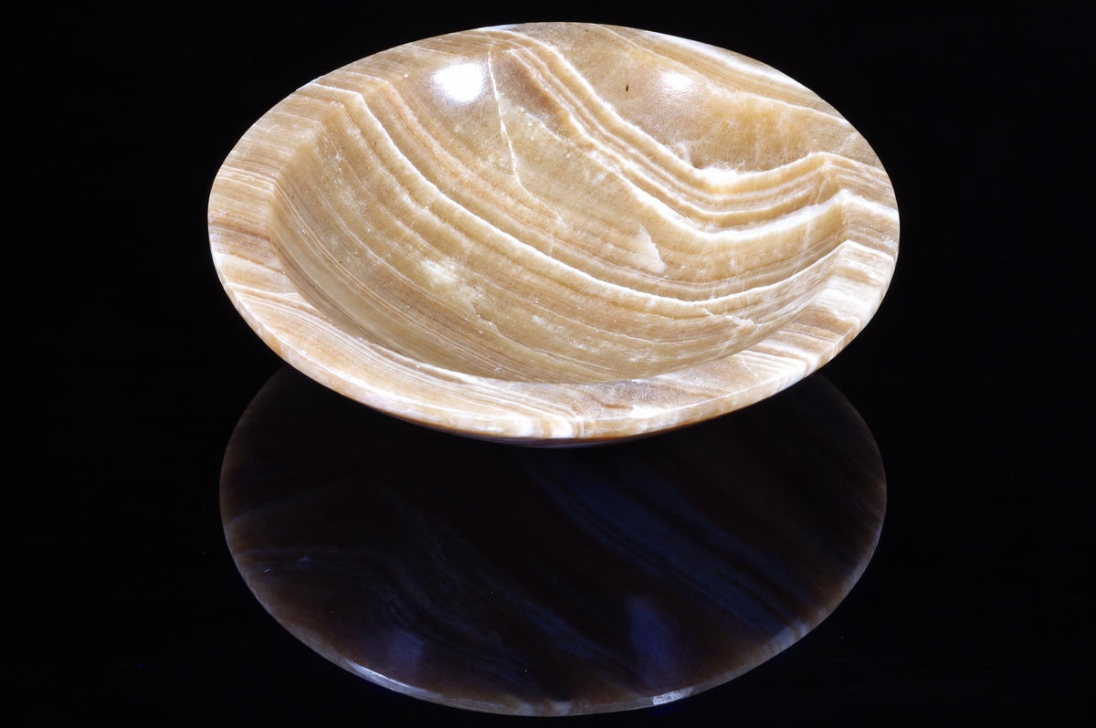 A polished, oval bowl with wavy beige and white stripes sits on a dark, reflective surface.