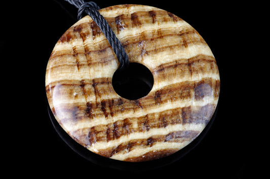 A polished, donut-shaped pendant with brown and cream striped patterns on a dark surface.