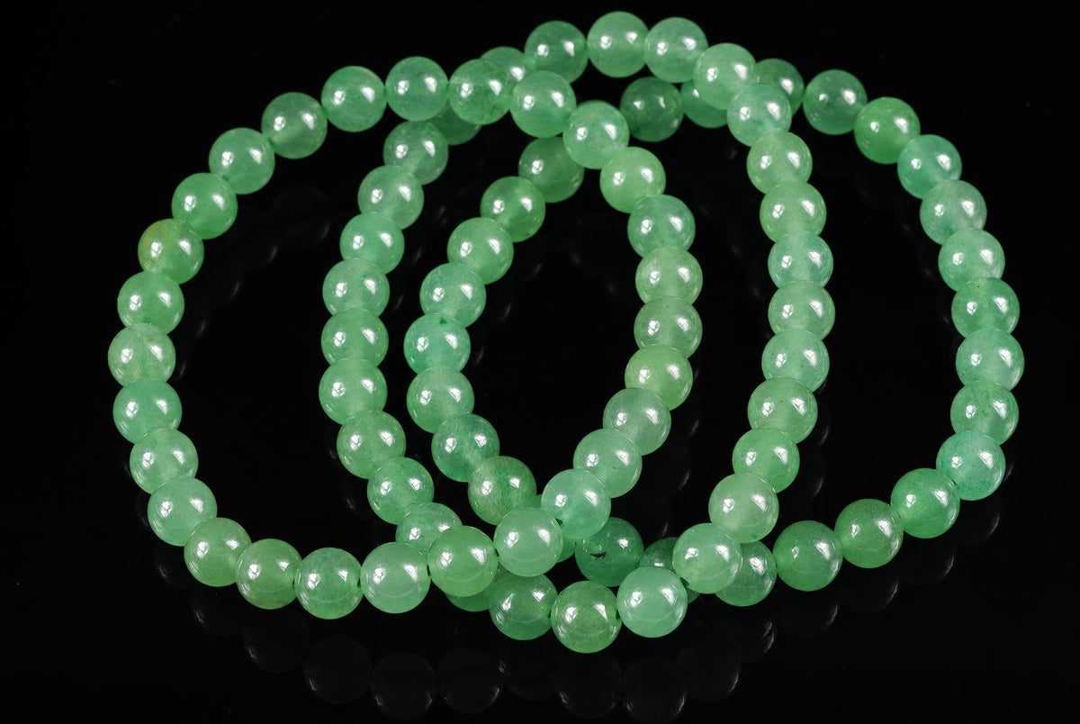 A bracelet of round, light green aventurine beads arranged in loops on a dark surface.
