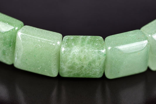 A close-up of a bracelet with square, light green aventurine beads on a dark surface.