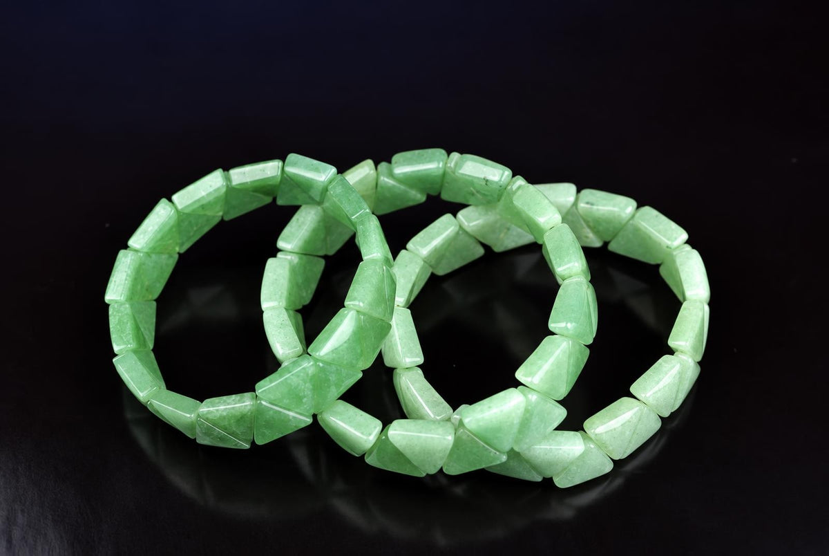 Three light green Aventurine bracelets with triangular beads arranged on a dark surface.