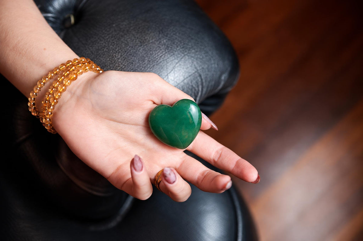 A hand holds a polished green aventurine heart against a softly blurred background.