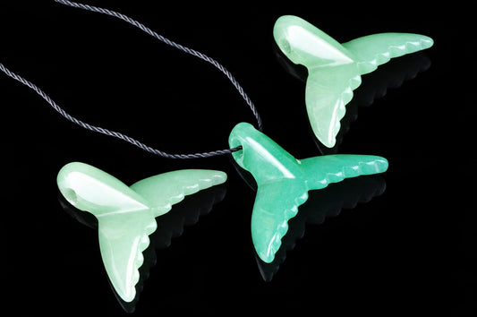 Three green aventurine dolphin tail pendants on a dark surface, each attached to a twisted cord.