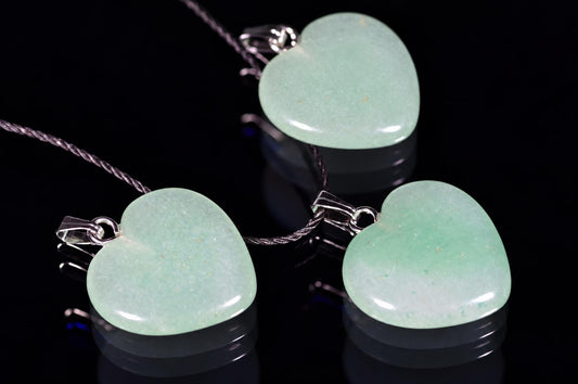 Three heart-shaped aventurine pendants in pale green, each with a silver-toned bail and cord chain on a dark reflective surface.