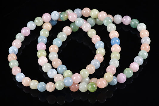A beryl bracelet with round beads in pastel pink, blue, green and peach on a dark reflective surface.