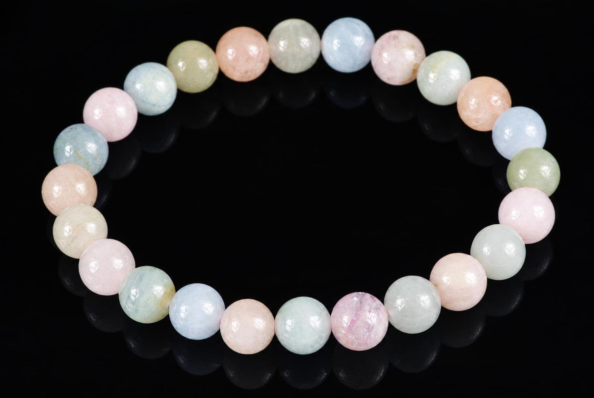 A bracelet of round beads in pastel pink, blue, green and peach on a dark surface.